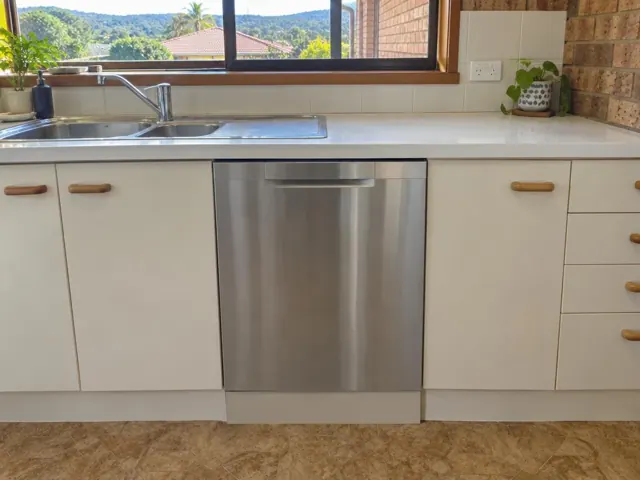 Stainless dishwasher installed under a kitchen benchtop with cream cabinets and tiled splashback in Gateshead