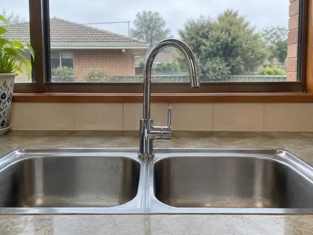 Chrome kitchen mixer tap over a double stainless sink with tiled splashback and window in Bennetts Green