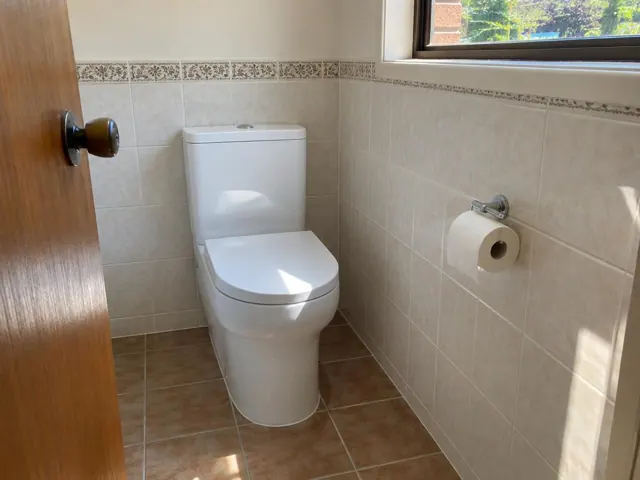 White toilet installed in a tiled bathroom beside a window and paper holder in Whitebridge